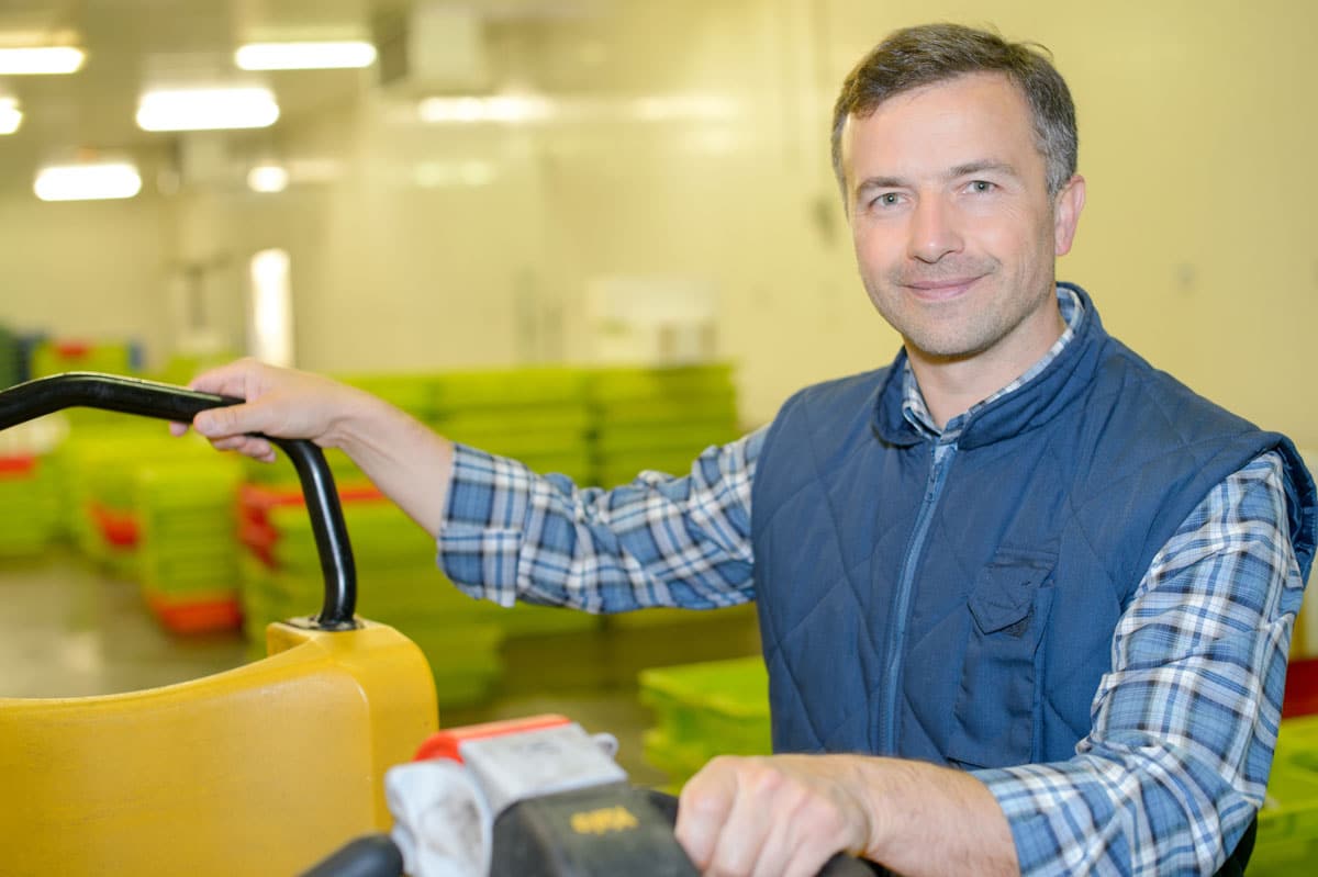 Man working in cold storage facility smiling while operating warehouse equipment